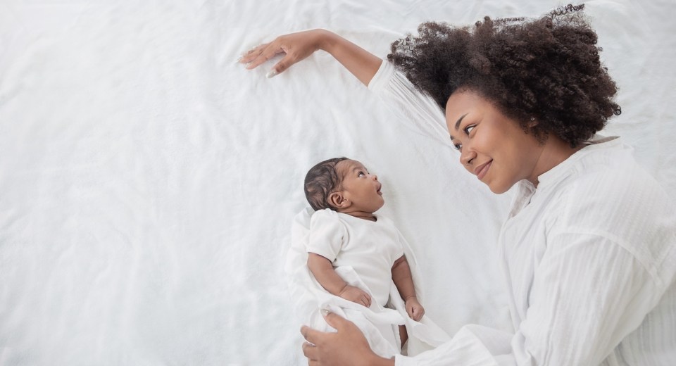 How to reclaim your confidence after having kids Mother bonding with baby on a white bed, smiling with love, symbolizing how to reclaim your confidence after having kids.