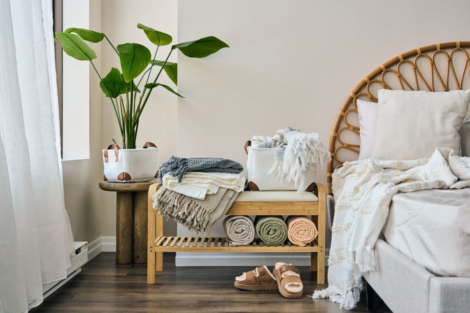 A cozy, modern bedroom features a wood bench stacked with soft, neutral-colored sheet sets and throws, highlighting the perfect sheet sets for comfort and style.
