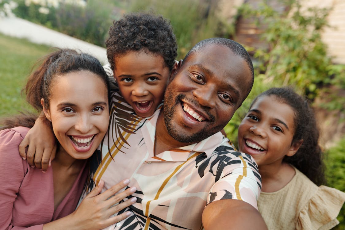 Smiling black family taking a cheerful outdoor group selfie during family adventures.