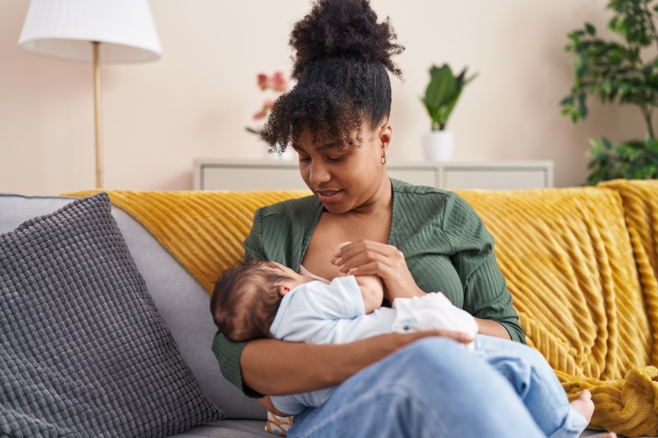 An african american mother breastfeeds her baby while sitting on the couch for an article about breastfeeding transfers essential antibodies from mother to baby, boosting the infant's immune system and protecting against illnesses until they're ready for vaccinations.
