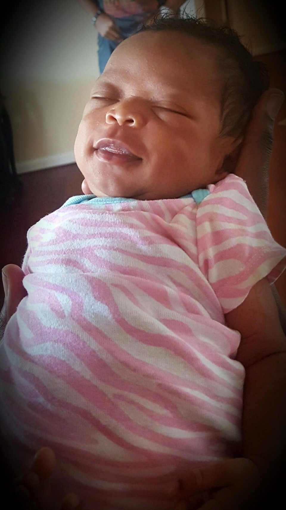 Newborn baby smiling peacefully in pink zebra onesie, held with love for an article about black, single, and proud: why more black women are choosing motherhood on their own terms.