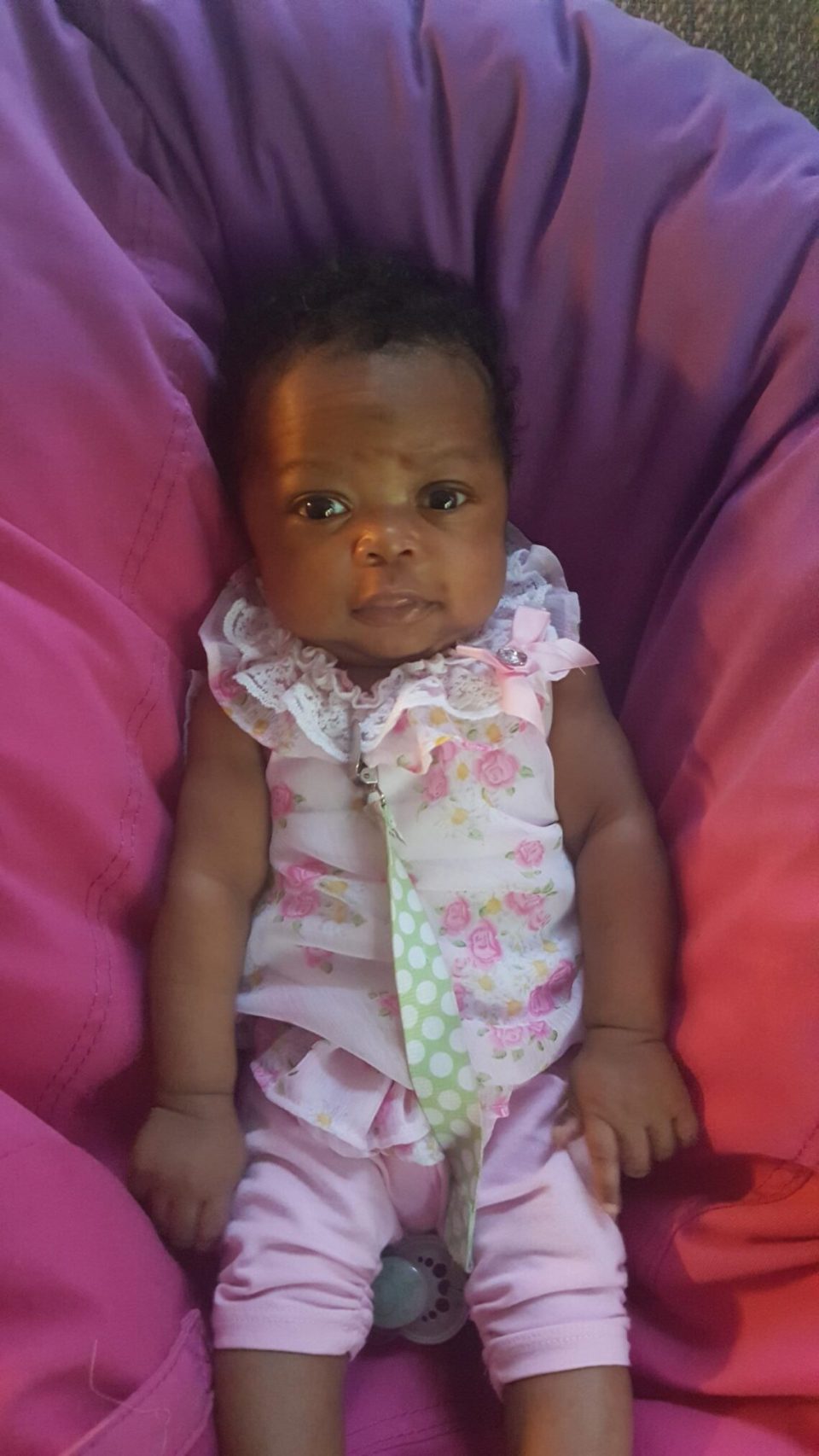 Baby in floral outfit lying on purple pillow, bright-eyed and content for an article about black, single, and proud: why more black women are choosing motherhood on their own terms.