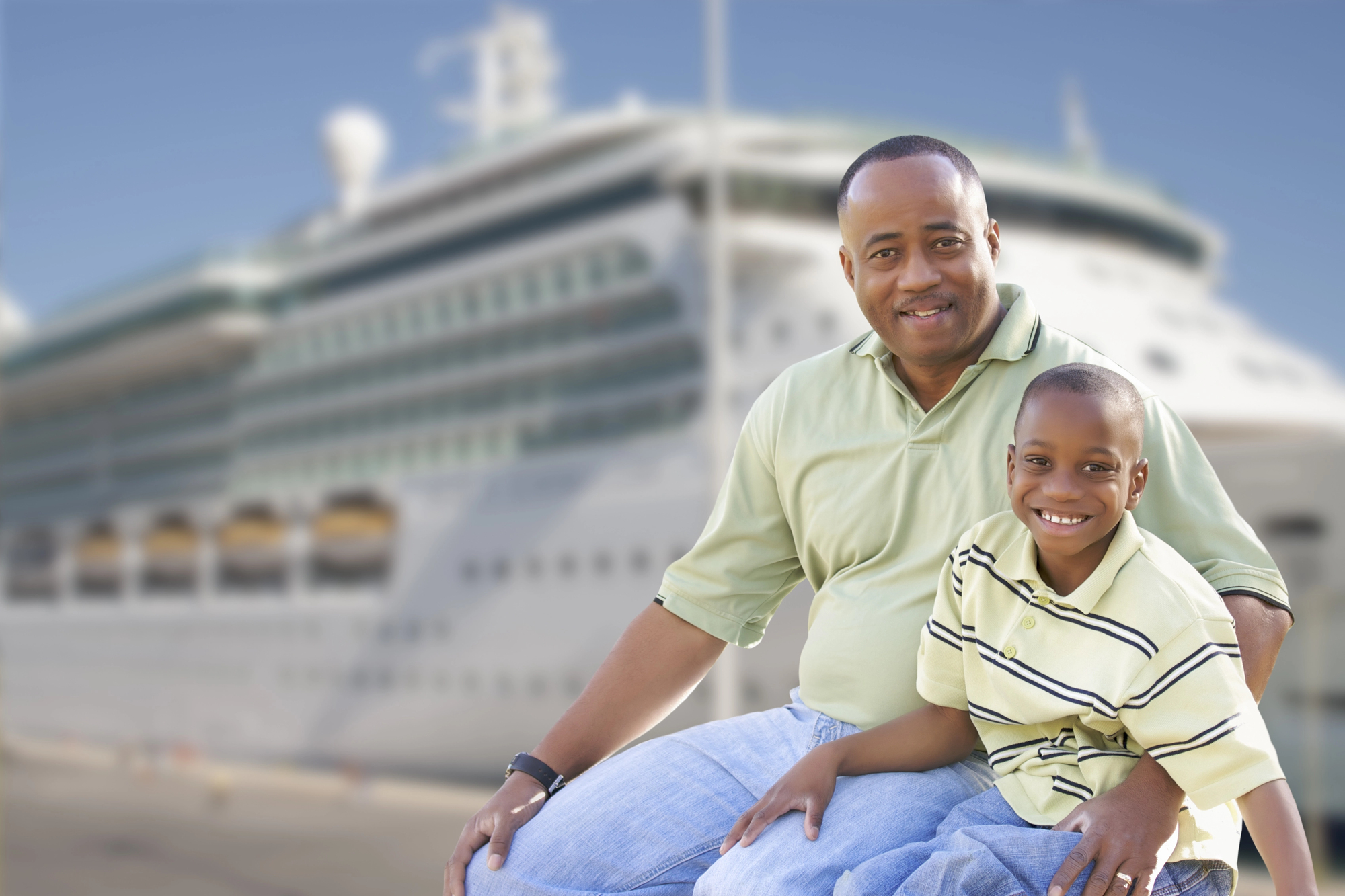 Black father and son smiling together in front of cruise ship, representing joyful travel moments with a child with autism – traveling with a child with autism