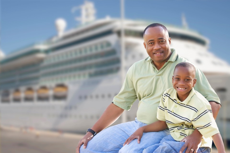 Black father and son smiling together in front of cruise ship, representing joyful travel moments with a child with autism – traveling with a child with autism.