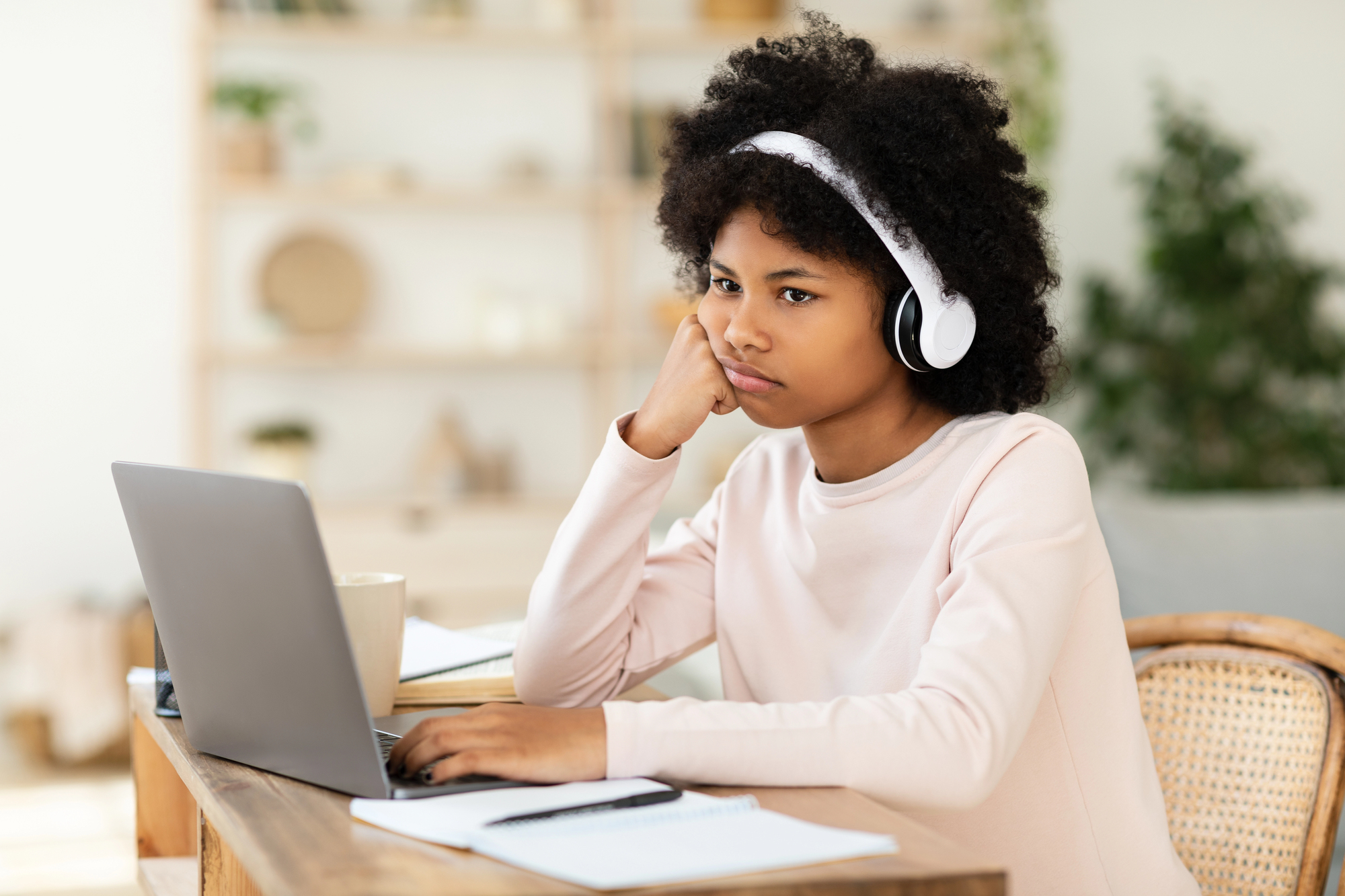 Supporting your child's mental health: overcoming stress, social media, and stigma in the black community A young black girl with curly hair wearing headphones, sitting at a desk looking stressed while working on her laptop. The image represents the pressures of social media and academic stress faced by black youth, highlighting the importance of mental health support.