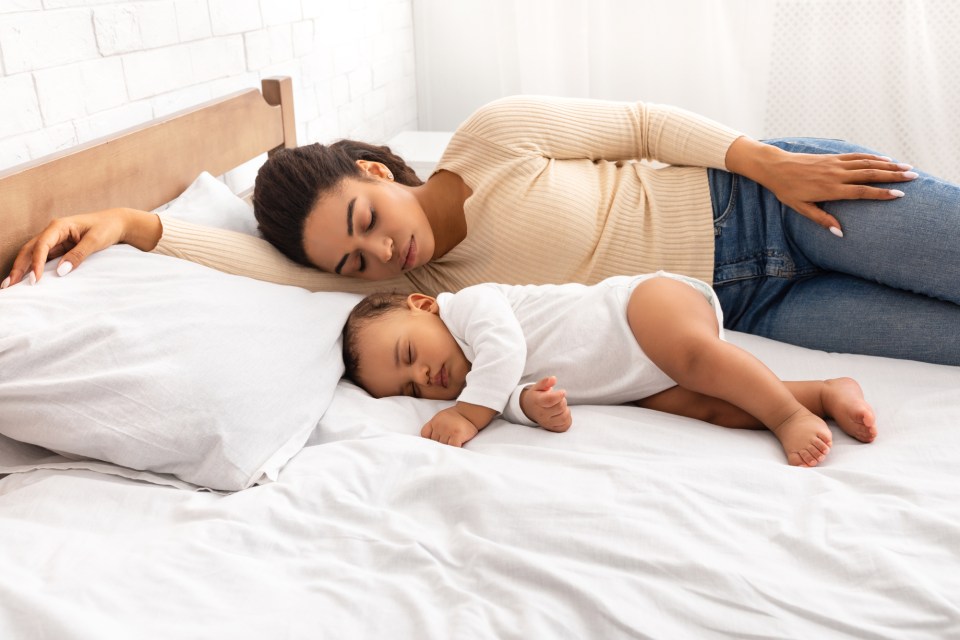 African mother and her baby son sleeping in bed indoor for an article about the redefined rest: how motherhood changes your relationship with sleep