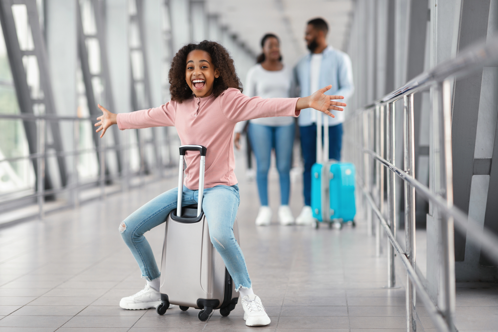 Smiling child riding a suitcase at the airport while traveling with parents, illustrating safe travels with kids on a worry-free family vacation.