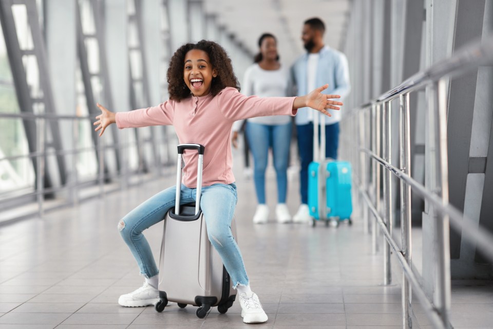 Safe travels with kids: your ultimate guide to ensuring a worry-free vacation Young girl riding a suitcase at the airport with her parents in the background, perfectly capturing the joy of safe travels with kids during a family vacation.