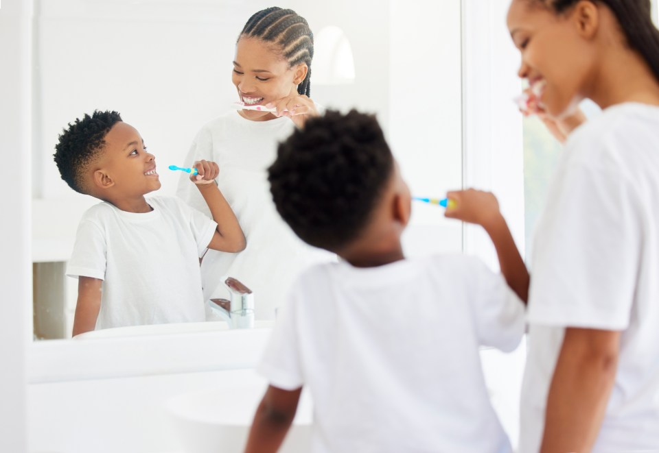 Caring for your family’s teeth: a parent’s guide An african american mother and son brush their teeth together in a mirror to care for their family's teeth as part of a parent's guide.