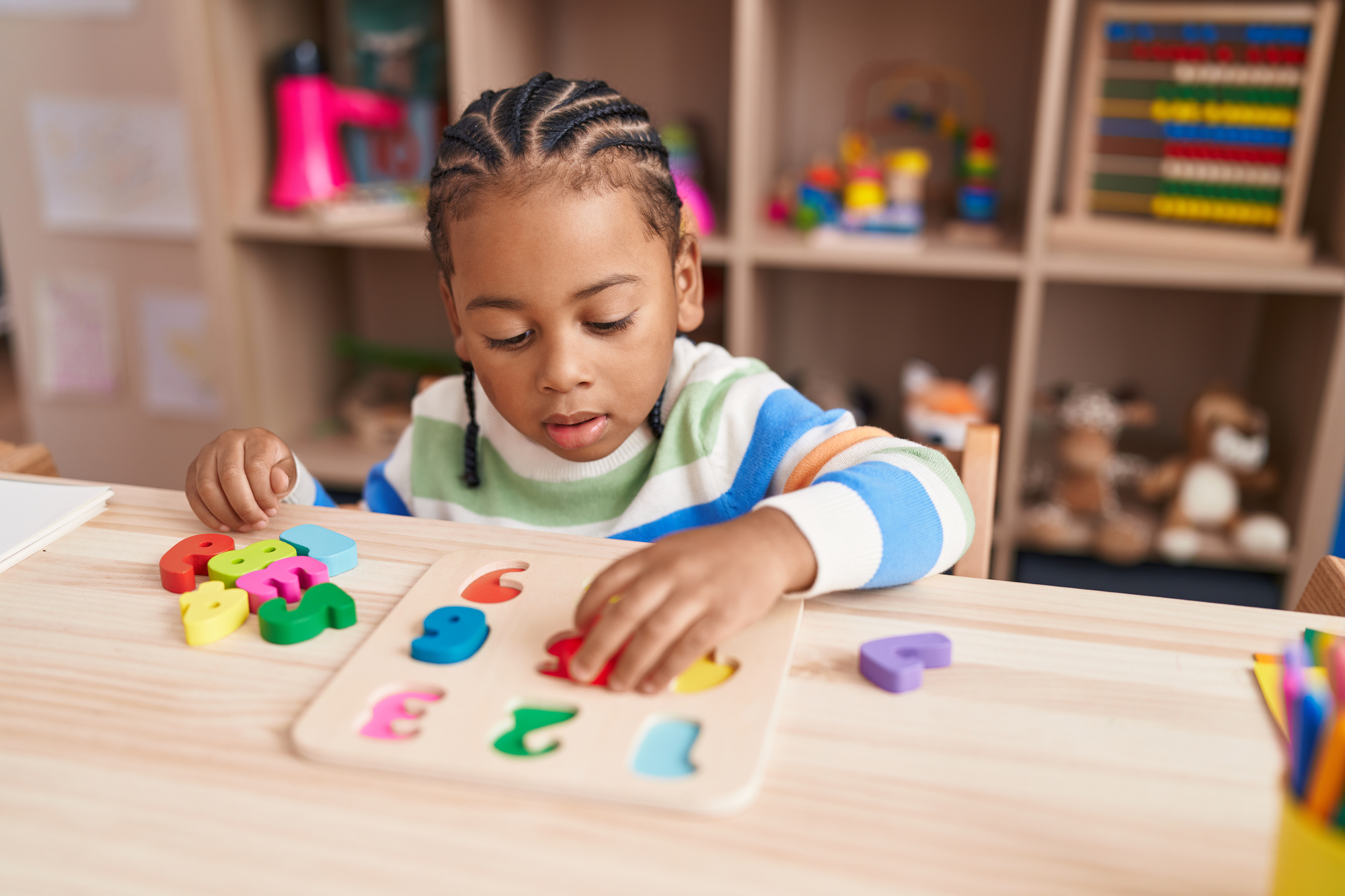 Busy boards – educational wooden toys for children African american boy playing with wooden toys and a puzzle game sitting on table at kindergarten