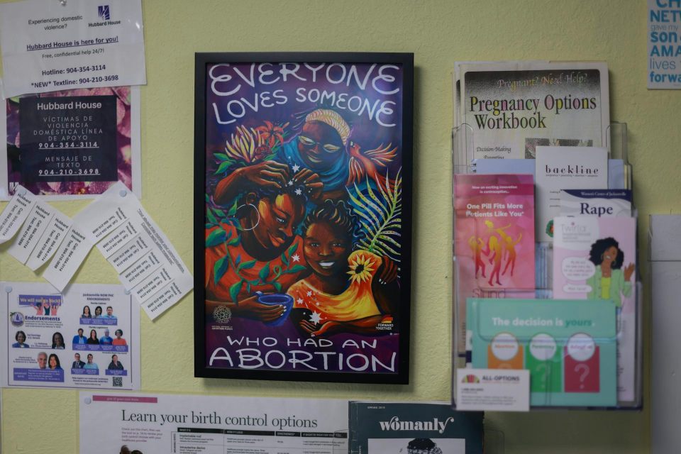 A colorful poster says 'everyone loves someone who has has an abortion,' and is surrounded by other papers on a wall.