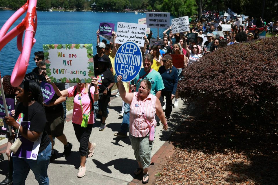 People walk as a group in front of water and hold signs that say 'keep abortion legal. '