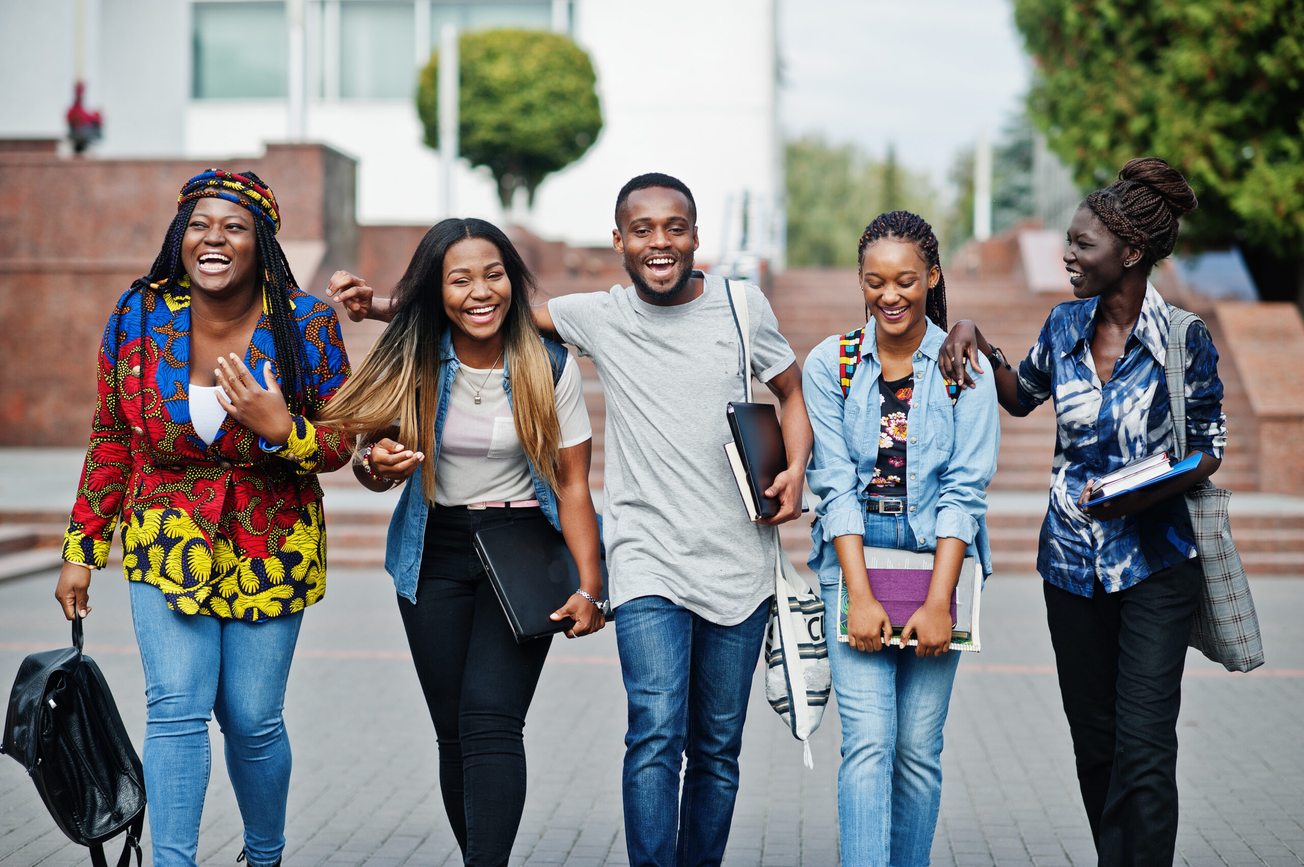 Group of five african american college students walking together on campus, smiling and holding books, representing academic success, friendship, and higher education for an article about 10 study habits that set kids up for long-term success.