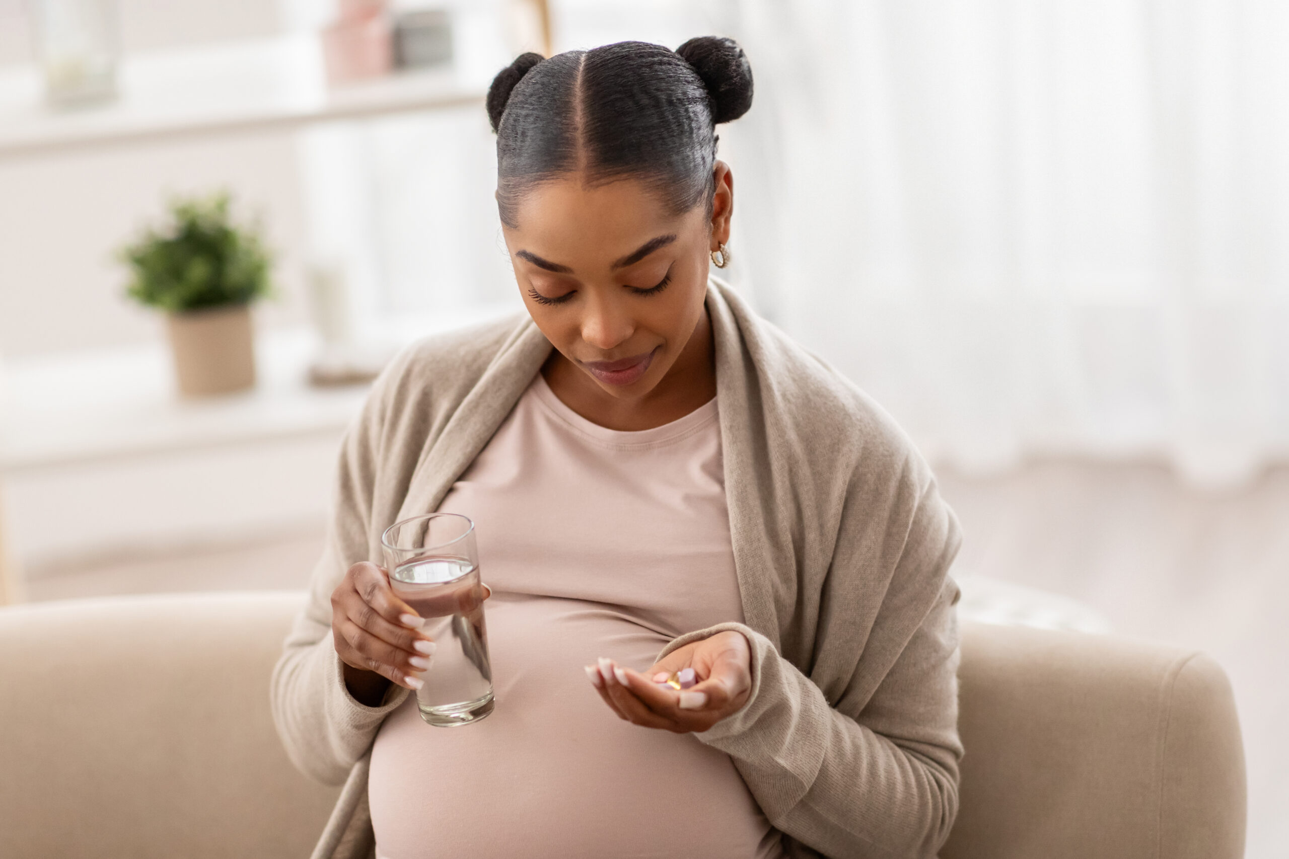 An african american woman takes her prenatal vitamins support. She is holding a glass of water and pills.