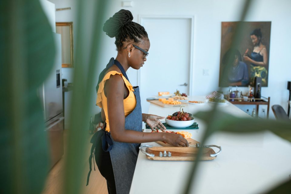 Black woman preparing food in a modern kitchen while running a home-based catering service, demonstrating one of the 7 essential tips for success for an article titled, "7 essential tips for running a home-based catering service. "
