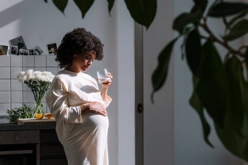 Pregnant black woman drinking water in kitchen showing how pregnancy can impact existing back problems and the importance of healthy posture
