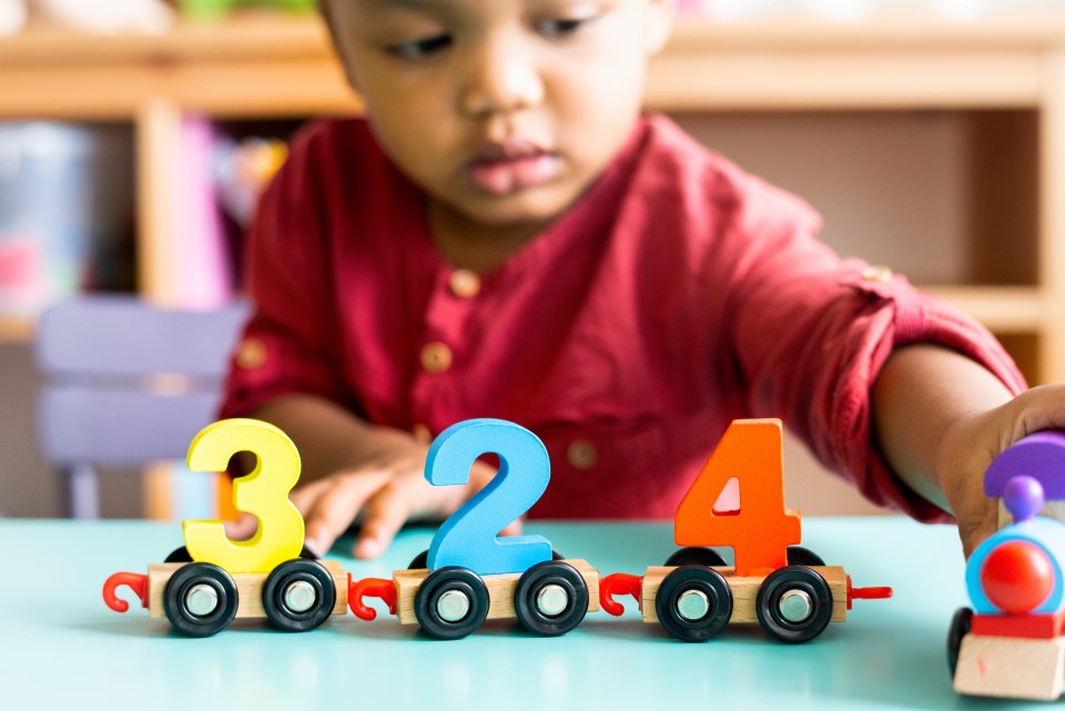 Black preschooler playing with colorful number toys in a sensory-rich classroom in aventura, focused on learning through play for an article about how sensory-rich classrooms in aventura encourage expression in young learners.