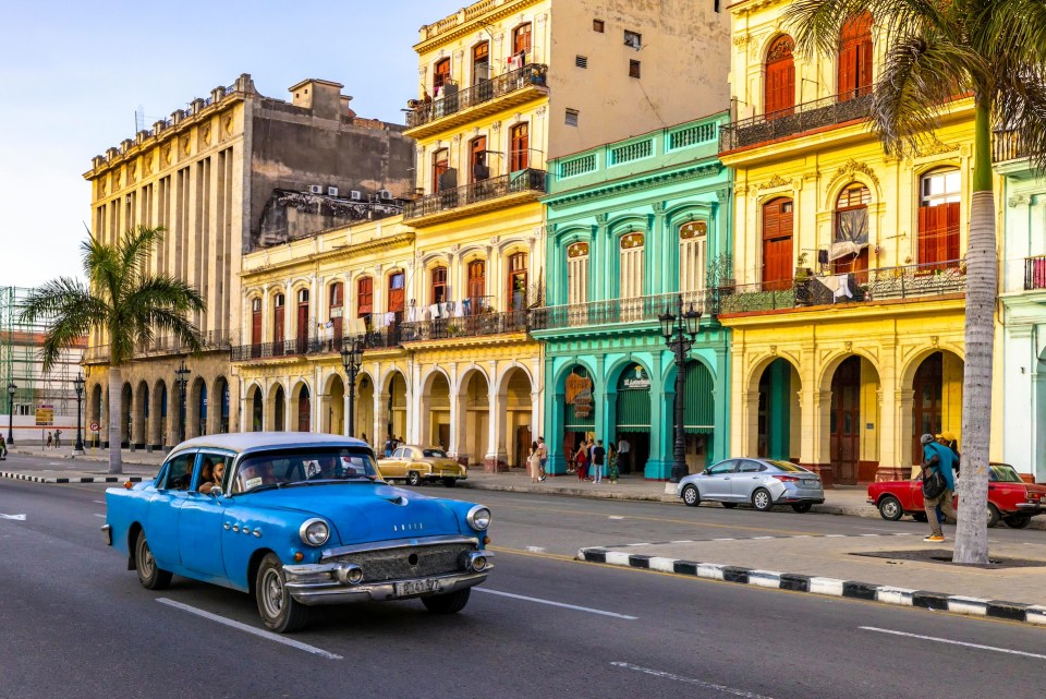 Colorful buildings and a classic blue car on a street in cuba, vibrant family travel spot.