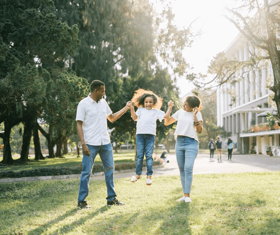 Black parents swinging their child joyfully in a sunny park, representing family unity and the importance of child well-being in family court custody decisions.