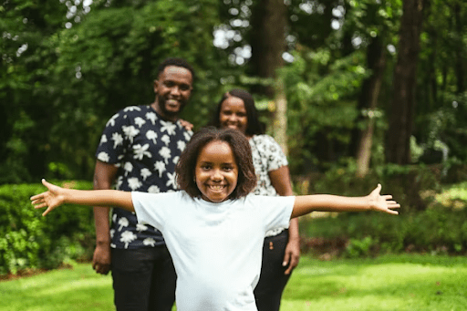 5 reasons black american parents are choosing boarding schools for their kids' future Smiling black girl with arms wide open in front of her proud parents outdoors, representing black american families exploring boarding school options for an article about 5 reasons black american parents are choosing boarding schools for their kids' future