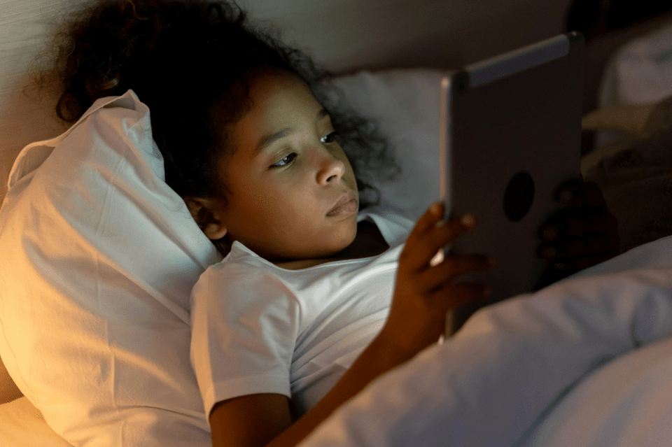 A little african american girl reads her tablet in her bed while digital landscapes.